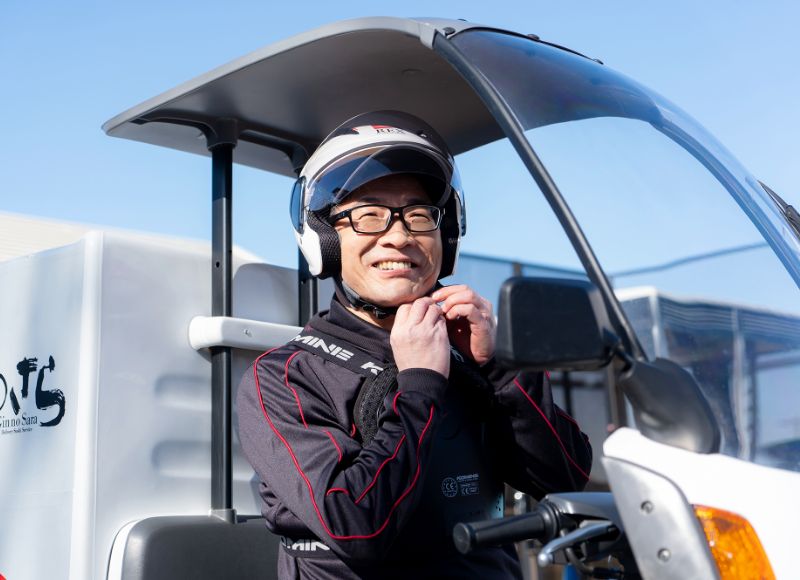 配達用バイクのそばで笑顔を見せるHさん